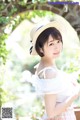 A woman wearing a straw hat standing in front of a tree.