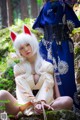 A woman in a kimono sitting on a rock in the woods.